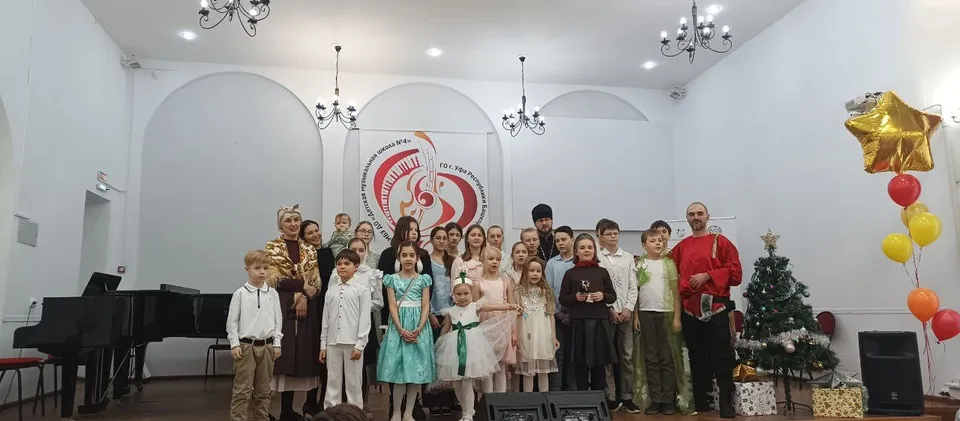 Дети в костюмах выступают на сцене на фоне новогодних украшений