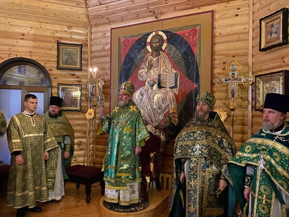 Архиерей со свечой стоит перед образом Спасителя, вокруг — сослужащее духовенство в зелёных облачениях